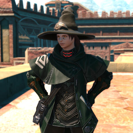 Kheda wearing a dark green coat over a black woven shirt. He has a large green hat. He stands with his hands on his hips wearing a stern expression. His eyes glow bright orange beneath the brim of his hat.