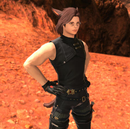 Kheda in a tight-fitting black sleeveless top. He wears gloves with a red accent, black belted pants, and black over the knee thighboots. He stands with his hands on his hips, staring off camera.