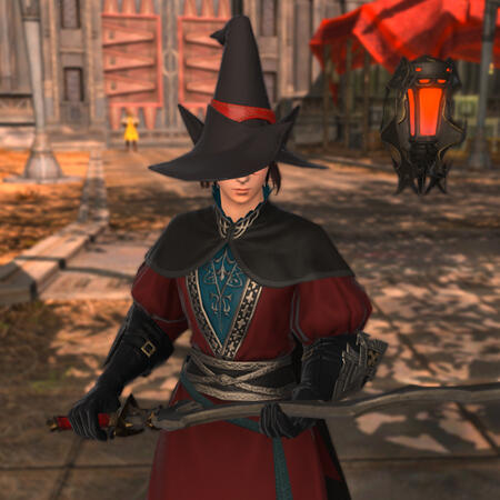 Kheda in a deep red and blue chasuble. He wears a large mage hat with a red ribbon, a black cape, and black gloves. He holds his rapier in a resting position, with one hand on the hilt and the other hand resting the blade in his palm.