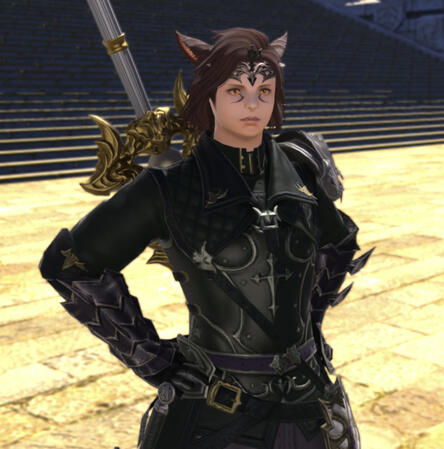Kheda stands with his hands on his hips staring forward with a stern expression. He wears fitted black armor that is belted around the middle, as well as gauntlets and a black circlet.