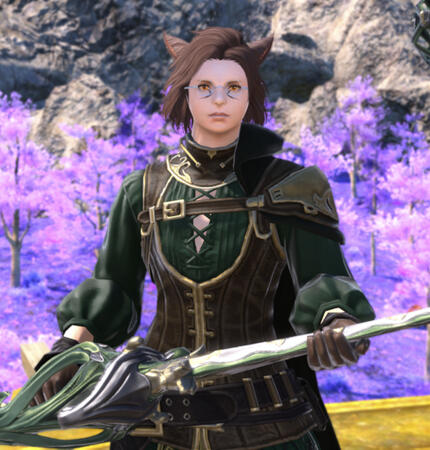 Kheda in a green skirt laced in the front, with a fitted brown vest layered over top. He wears a cape strapped to one shoulder, the strap extending across his chest. He balances his rapier between his hands, delicately holding it as he regards the viewer.